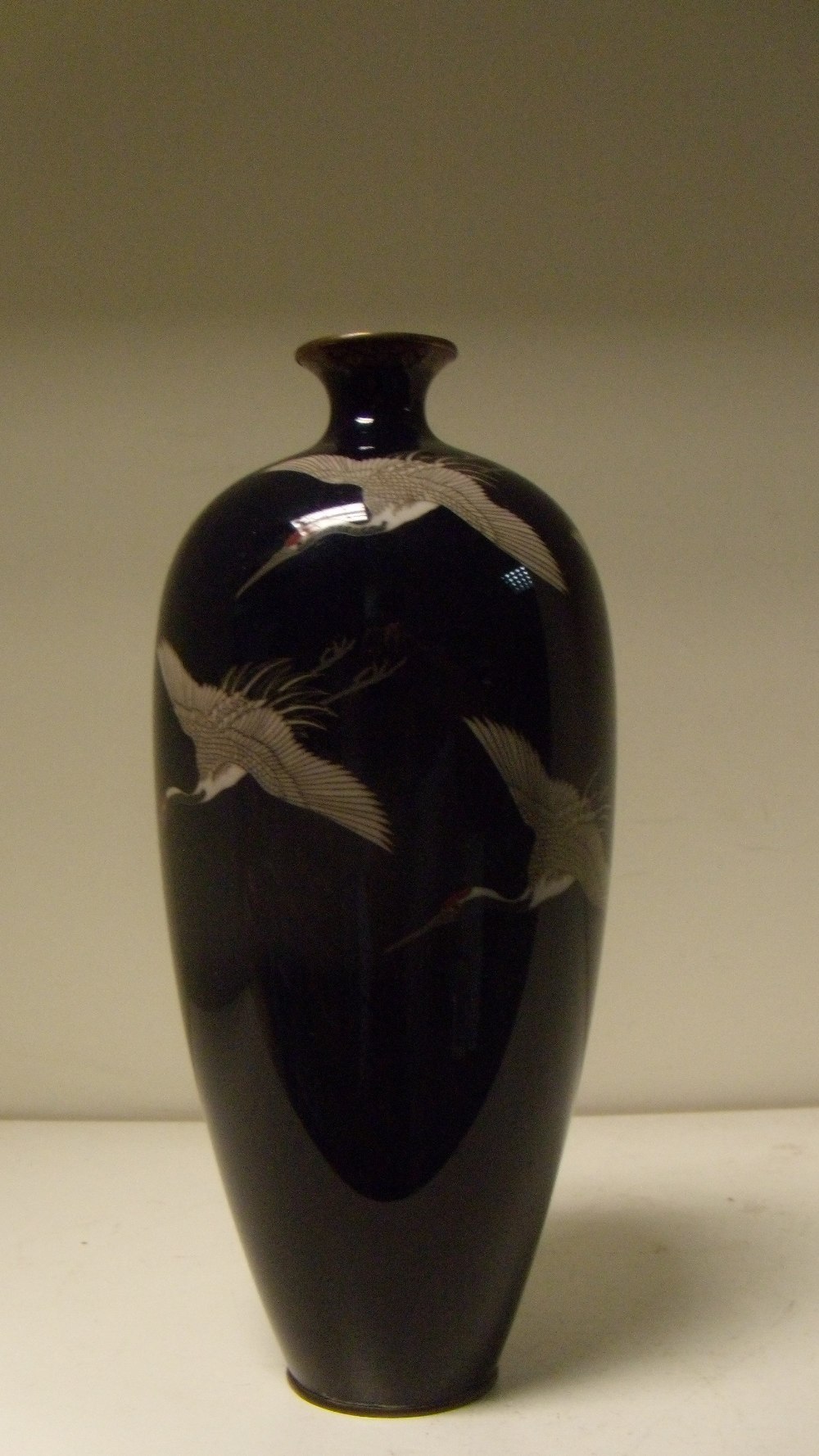 An early 20th century cloisonne vase, cranes flying down the slender ovoid body from the shoulders