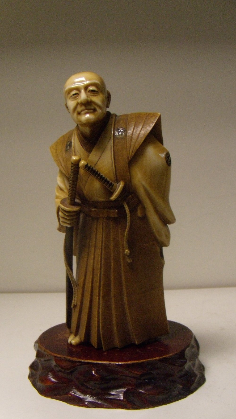 An early 20th century ivory figure of a samurai, the grey haired man wears a daisho with his