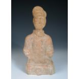 A Han dynasty red ware figure of a man seated crossed legged on a plinth, his hands resting on his