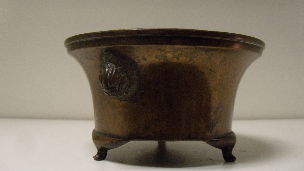 A 19th century bronze censer, the concave sides tapering to the three feet and applied with mask