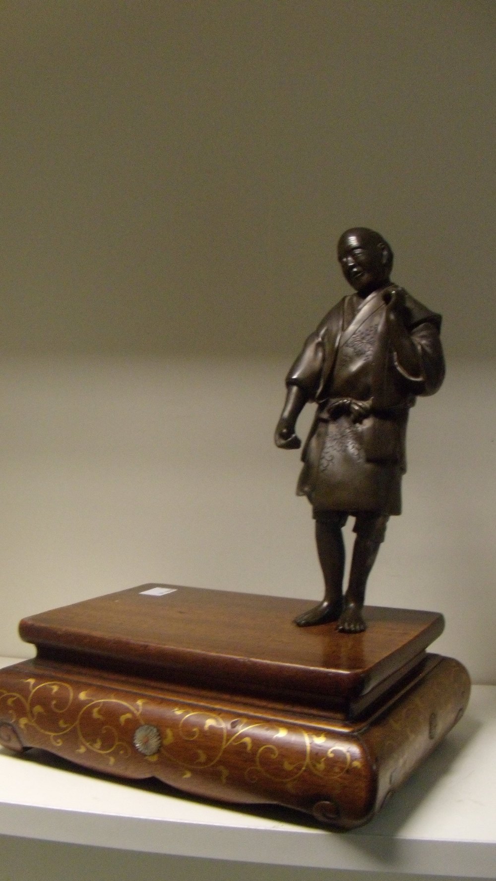 A late 19th/early 20th century bronze figure of a man standing to one corner of a wooden stand