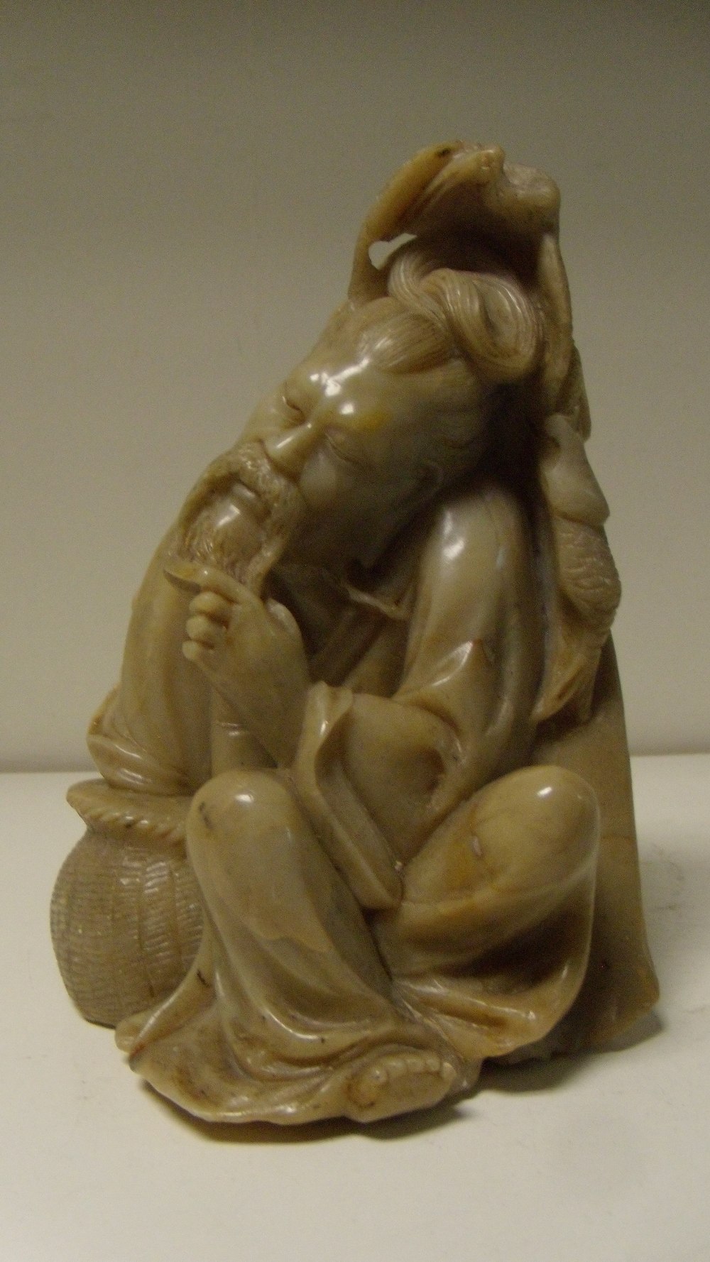 A buff grey soapstone figure of a fisherman, seated in a slumber, his left hand on his beard and his - Image 2 of 4