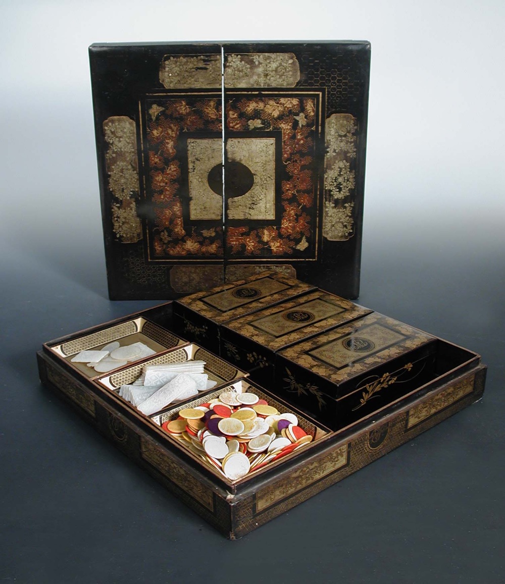 A mid 19th century black lacquer games box, gilt floral panels and grape vine bands enclosing the