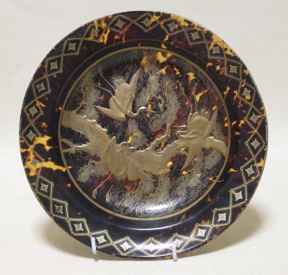 A faux tortoiseshell dish decorated in gilt with cranes within a geometric border, 26cm diameter