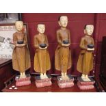 Four wooden figures of Buddhist monks standing with their begging bowls