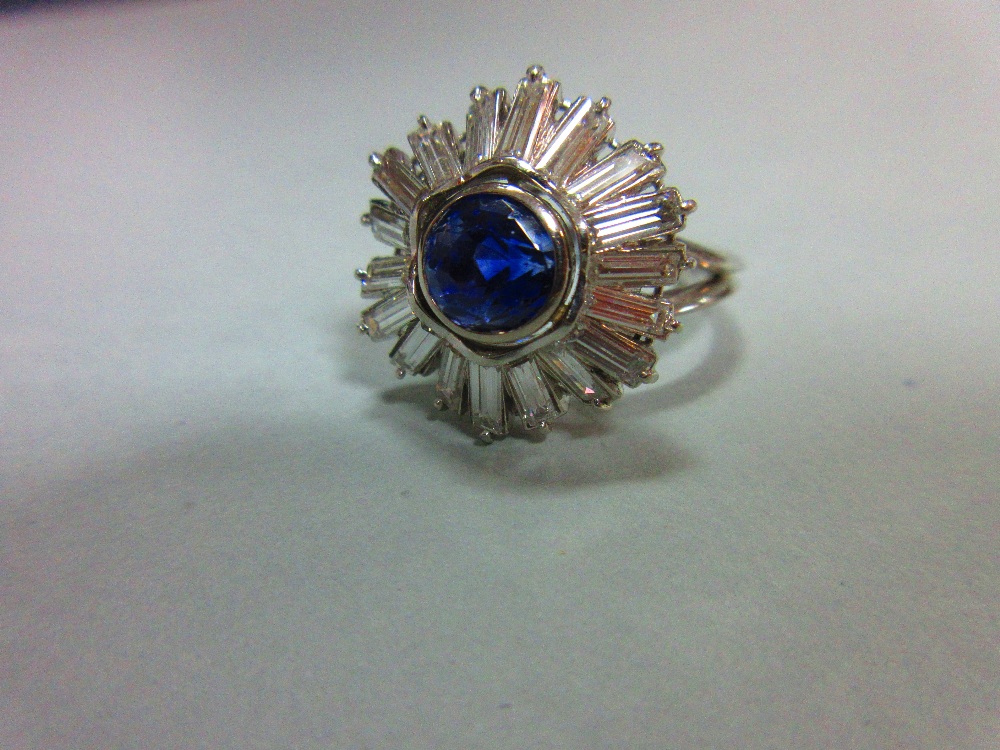 A sapphire and diamond sunburst cluster ring, the round cut light indigo coloured sapphire collet