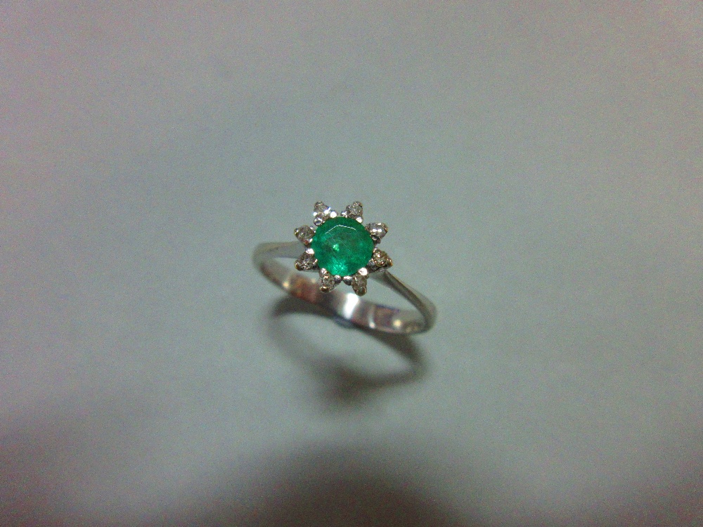 An emerald and diamond ring, set with a round cut emerald in a small petal border of eight single