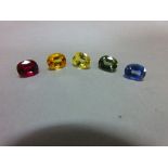 A loose ruby and four loose variously coloured sapphires, all oval to rectangular cushion cut and