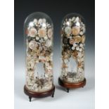 A pair of Victorian shell displays beneath glass domes, each worked with floral sprays in coloured