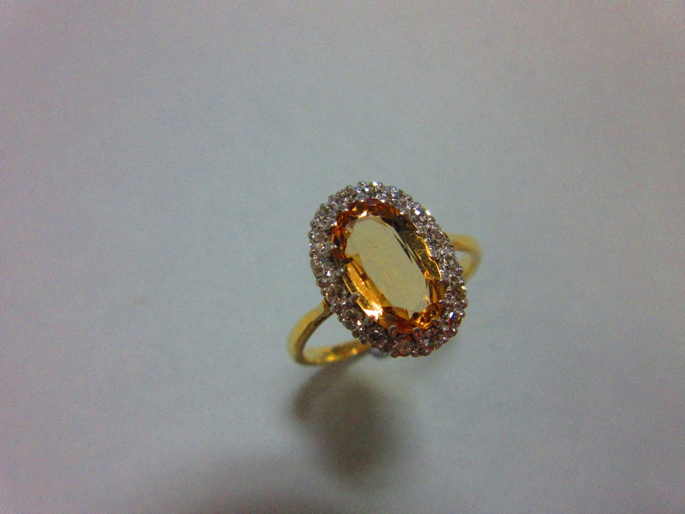 A topaz and diamond cluster ring, the oval cut light orange-brown topaz claw set in a border of