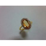 A topaz and diamond cluster ring, the oval cut light orange-brown topaz claw set in a border of