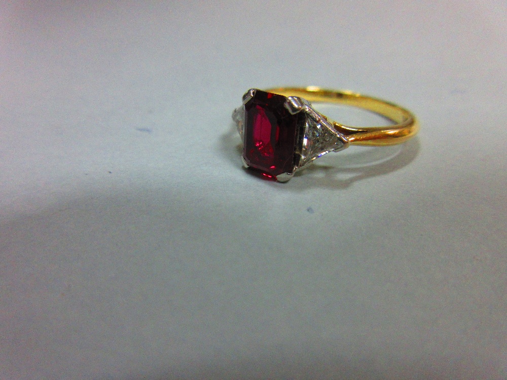 A ruby and diamond three stone ring, the emerald cut ruby four claw set between two trilliant cut - Image 2 of 4