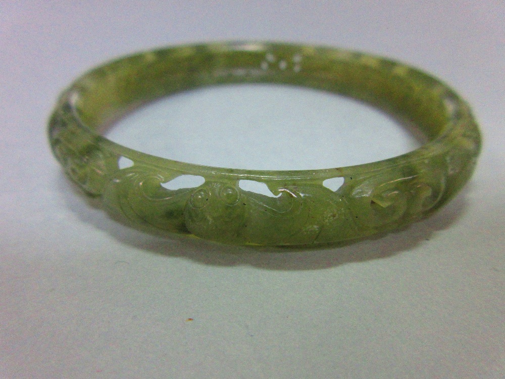 A carved jade bangle, the mottled light green jade of convex profile, pierced and carved with