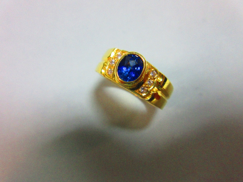 A sapphire and diamond ring, the oval cut intense blue sapphire in a raised collet between lines