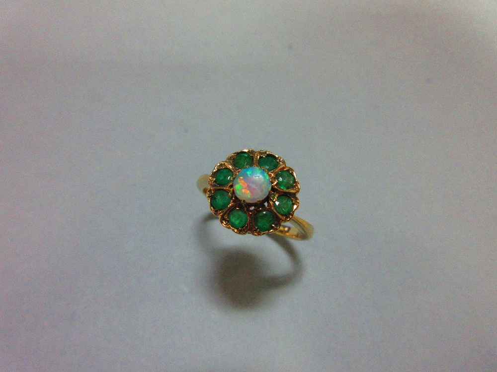 An opal and emerald cluster ring, with a round cabochon opal centre in a border of eight round cut