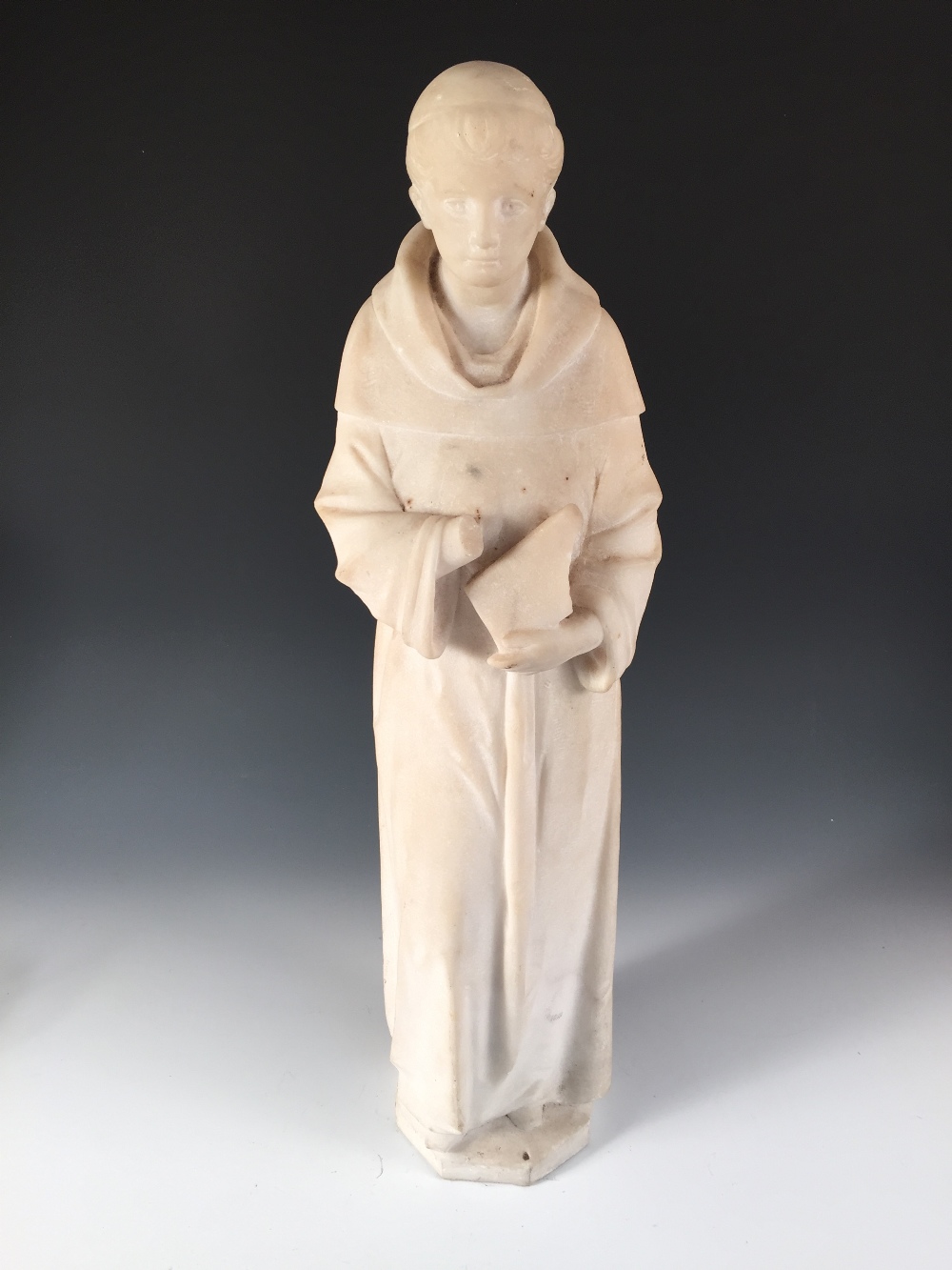 A 19th century white marble figure of a monk, the tonsured figure standing holding a book in his