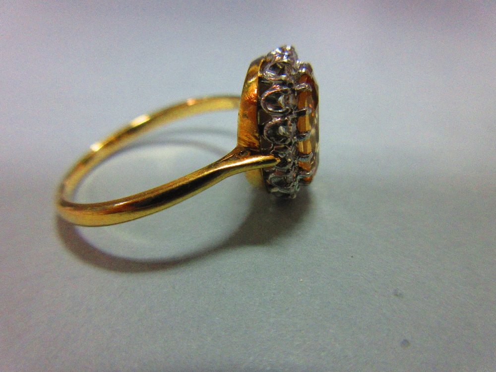 A topaz and diamond cluster ring, the oval cut light orange-brown topaz claw set in a border of - Image 3 of 5