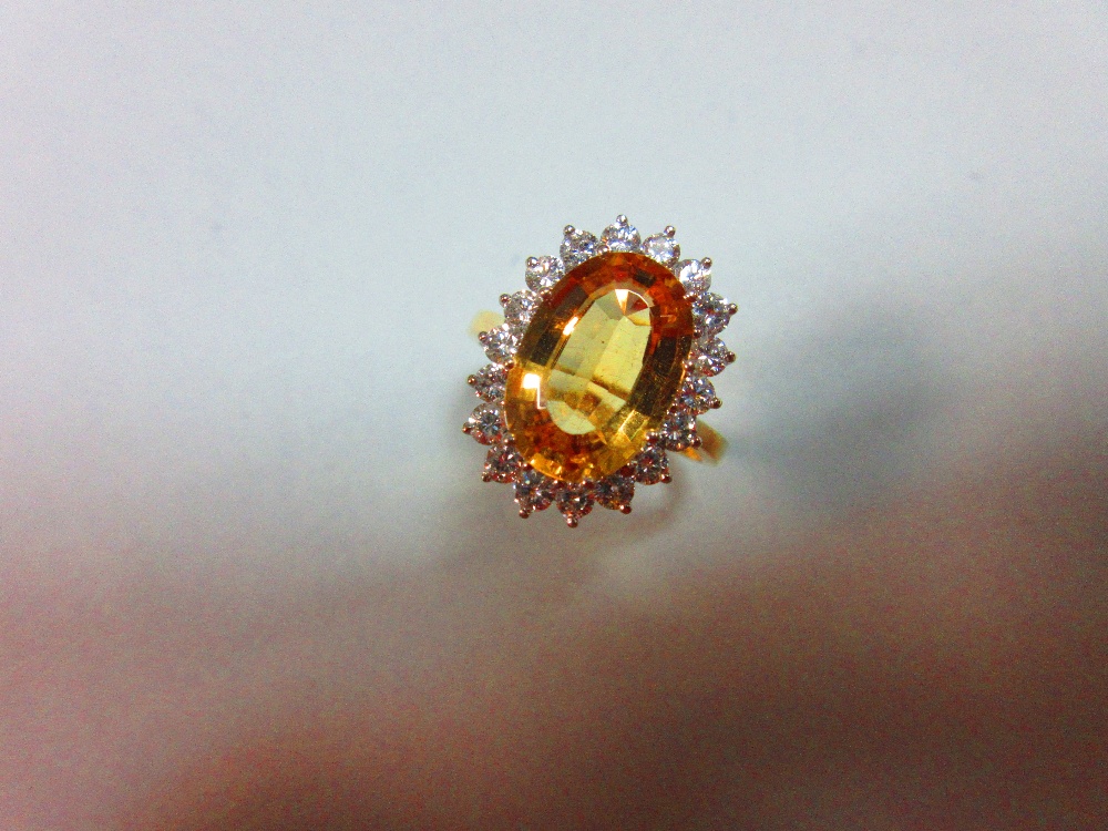 A topaz and diamond cluster ring, the oval mixed cut golden topaz claw set to a border of eighteen