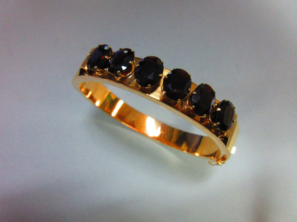 A 14ct gold and garnet hinged bangle, the polished gold hollow rectangular-section bangle, 9mm wide,