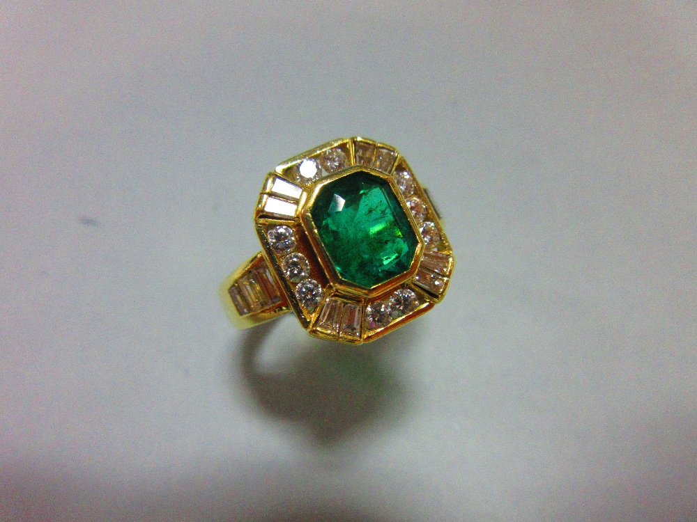 An Austrian 18ct gold emerald and diamond ring, the emerald cut emerald collet set in a border