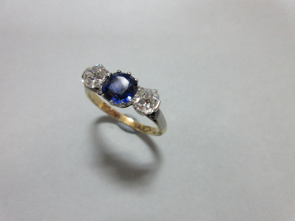 A three stone sapphire and diamond ring, claw set with a round cut royal blue sapphire between old