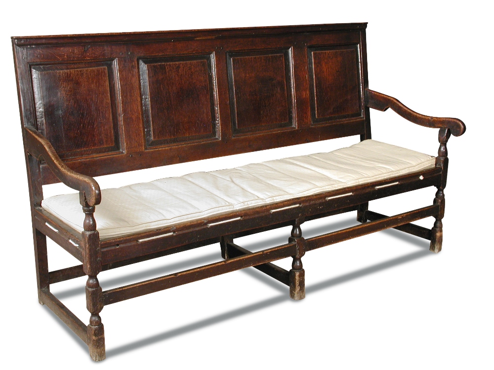 An early 18th century oak panelled settle, with open arms, strung seat and loose cushion, on