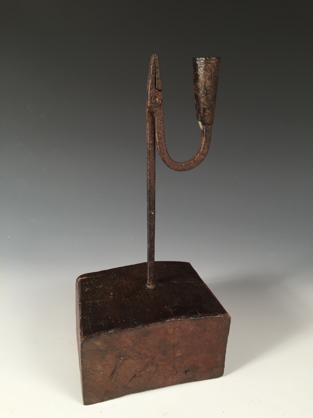 An 18th century iron rushlight holder with later wooden base, the square stem topped by a squared