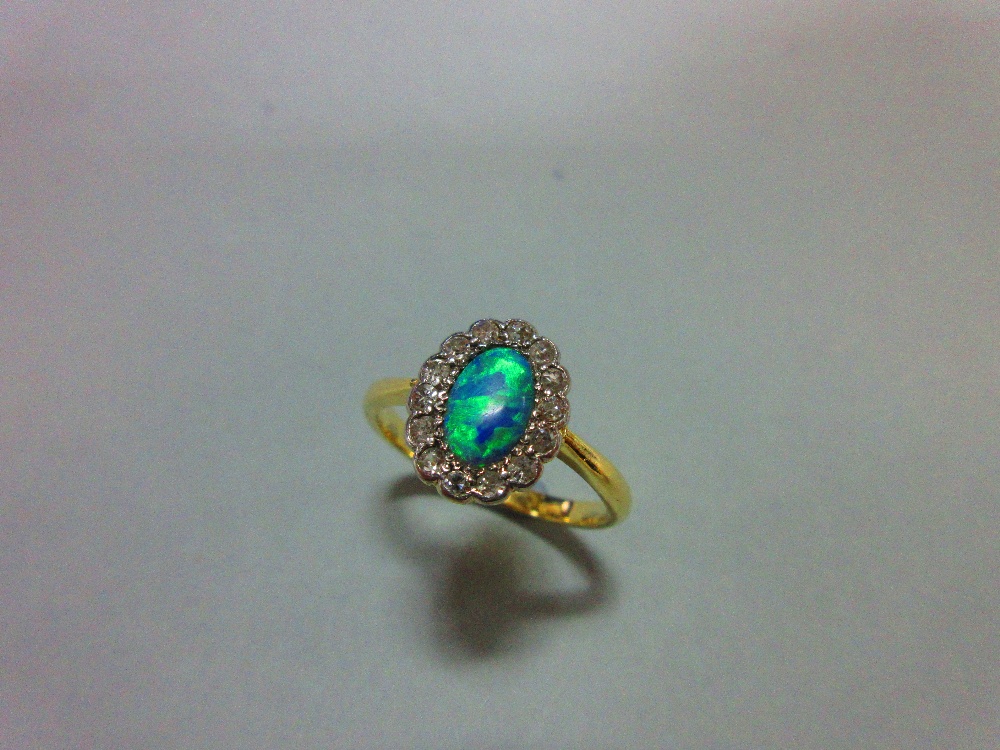 An oval opal and diamond cluster ring, the oval cabochon opal in a petal-edge border of single cut