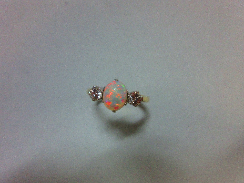 An opal and diamond three stone ring, the oval cabochon opal claw set between two round brilliant