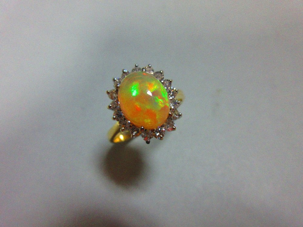 An opal and diamond cluster ring, the oval cabochon opal, displaying vivid predominently green and