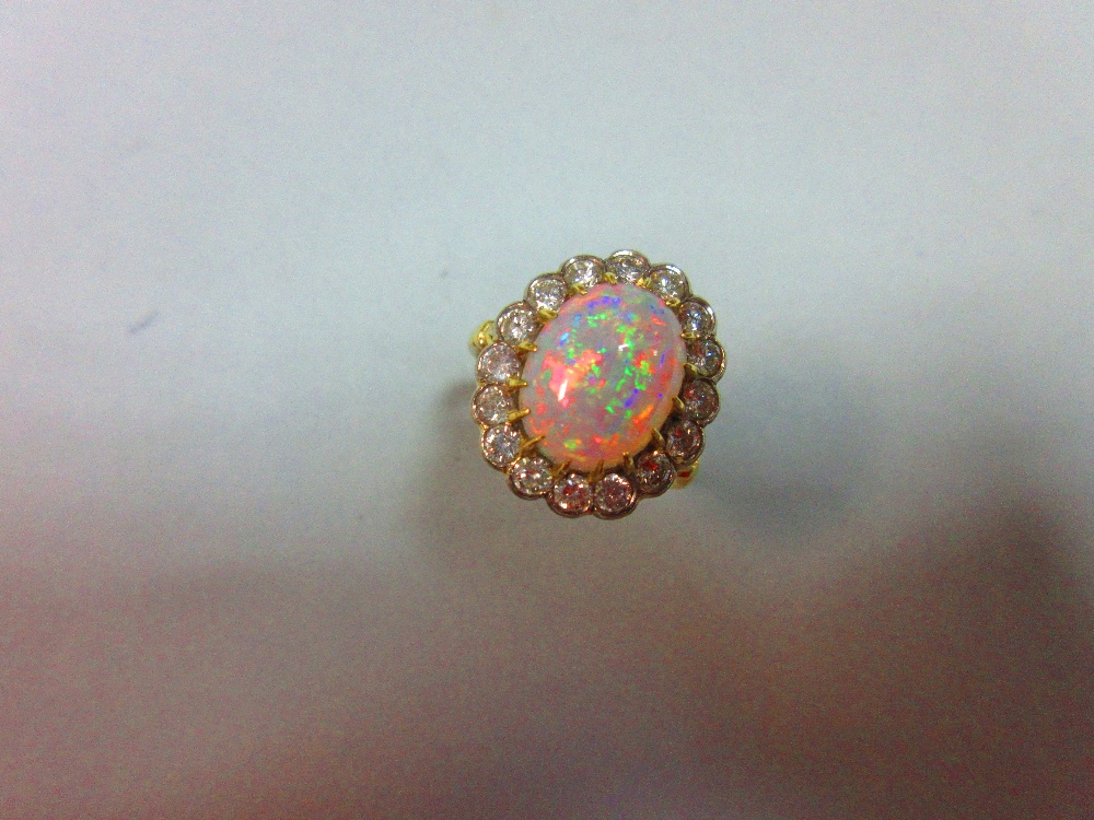 An opal and diamond cluster ring, the oval cabochon opal, displaying a rainbow range of fire, claw