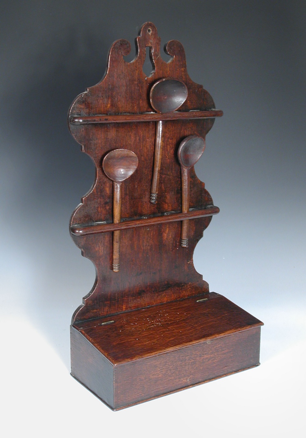 An 18th century oak spoon rack, the shaped back fitted with two pierced spoon rails above a hinged