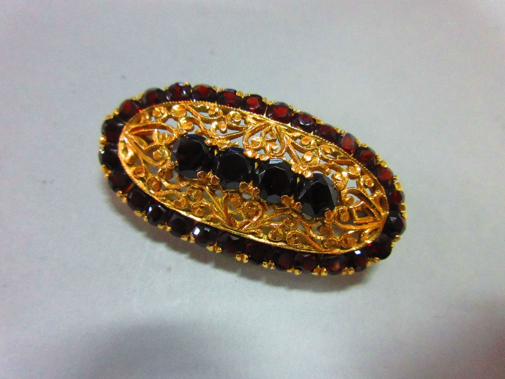 An Italian 18ct gold and garnet brooch, of elongated oval outline delineated by round cut deep red