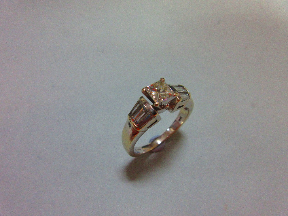 A contemporary princess cut diamond ring, the principal diamond four claw set to flying shoulders