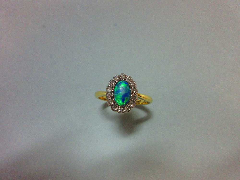An oval opal and diamond cluster ring, the oval cabochon opal in a petal-edge border of single cut - Image 2 of 5