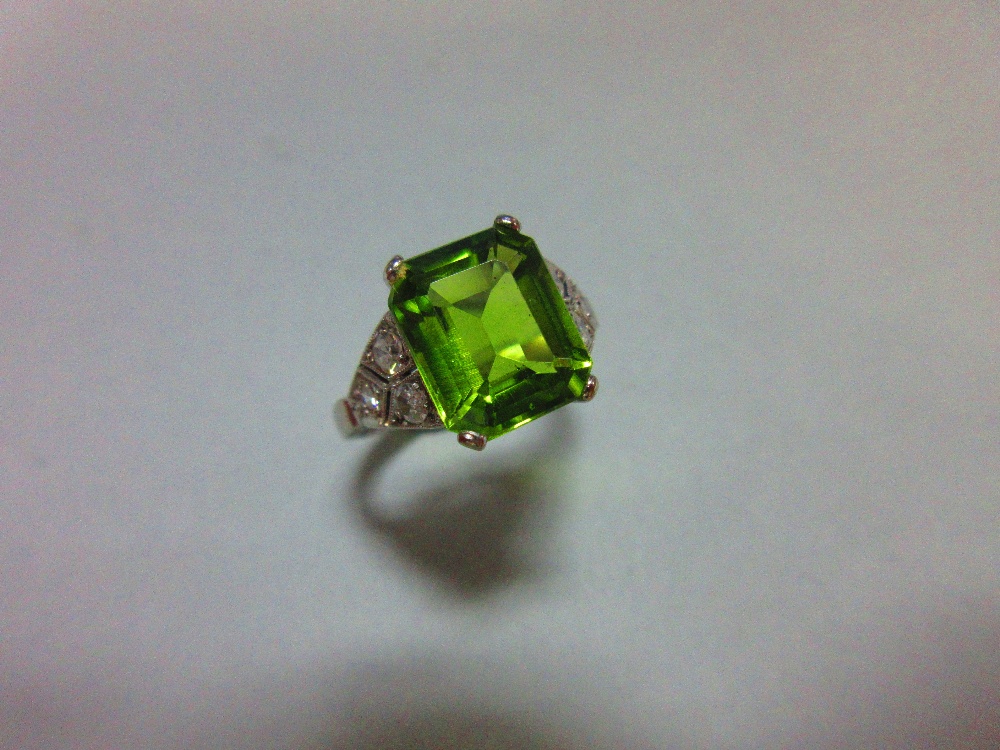 A 1930s style peridot and diamond ring, the emerald cut peridot measuring 10.6 x 8.7mm, four claw