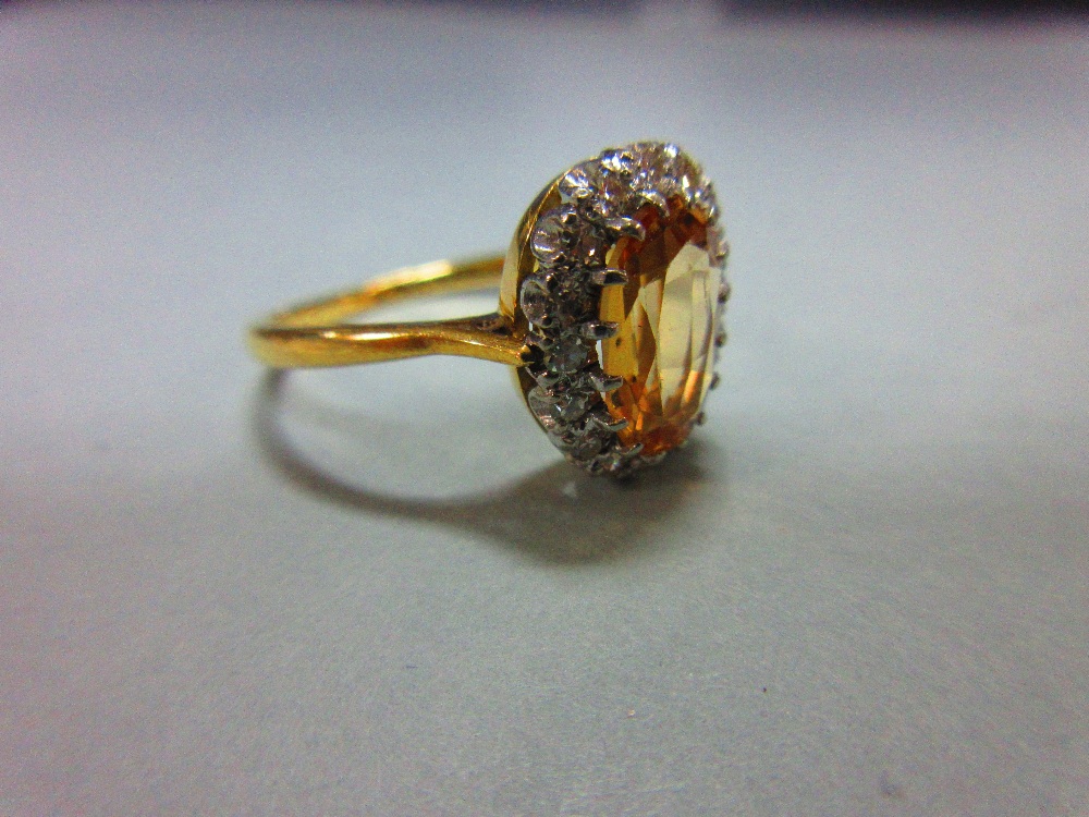 A topaz and diamond cluster ring, the oval cut light orange-brown topaz claw set in a border of - Image 2 of 5