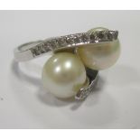 A two pearl and diamond ring, the two assymetrically set pearls supported by two rising prongs set