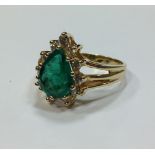 An emerald and diamond ring, the pear shaped emerald surrounded by small round brilliant cut