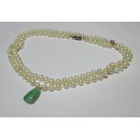 A cultured pearl necklace with a carved jade budha pendant 2cm long, together with a second strand