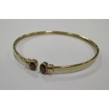 A yellow precious metal open ended bangle, set to ends with faceted oval garnets, cased