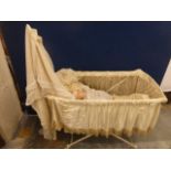 An Edwardian cradle with silk and lace drapes, containing a Pedigree plastic doll.