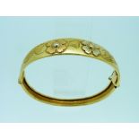 An 18ct yellow gold hinged Bangle, the shaped front engraved with two flower heads and leaves,