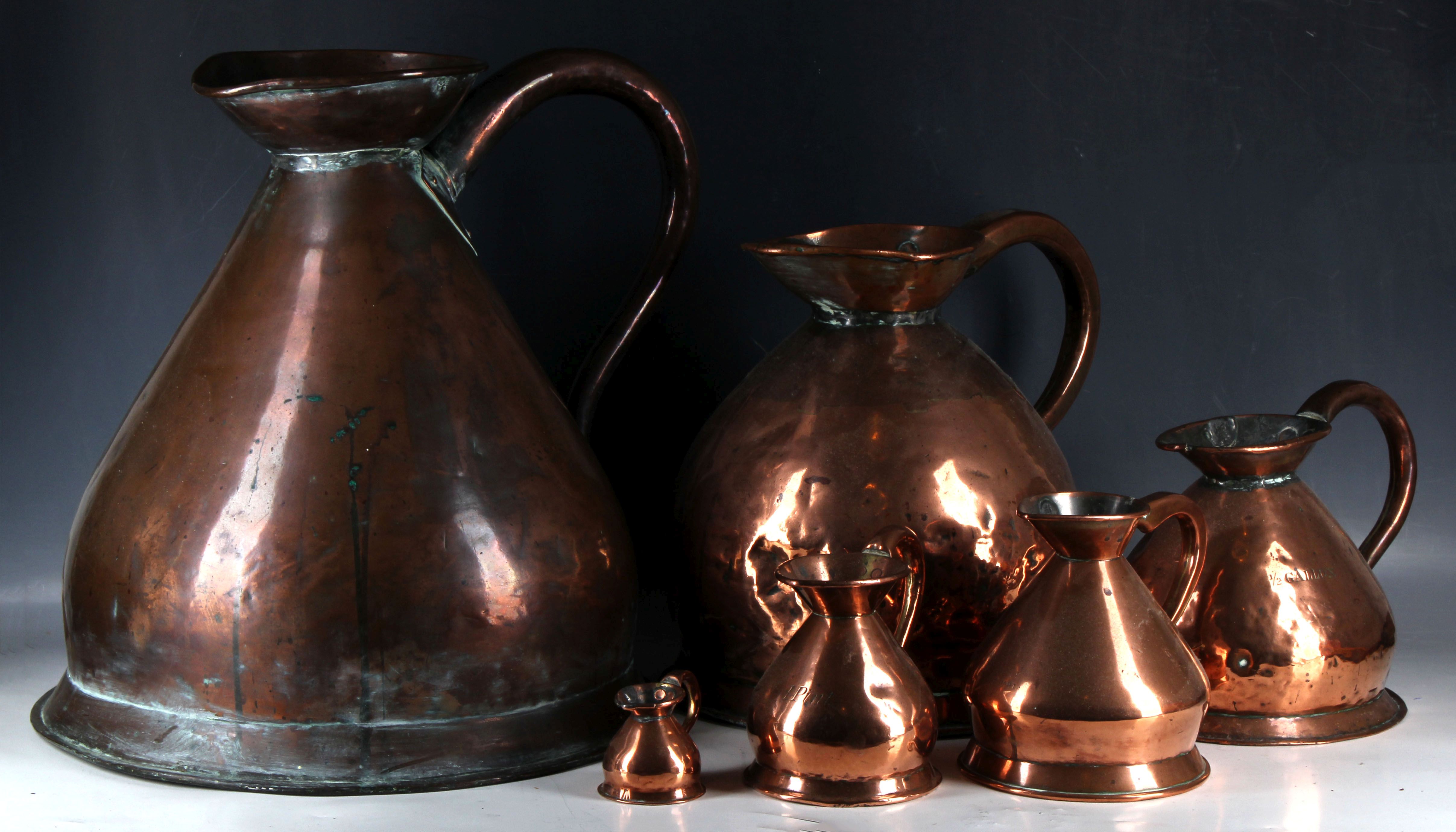 Seven copper measuring jugs.