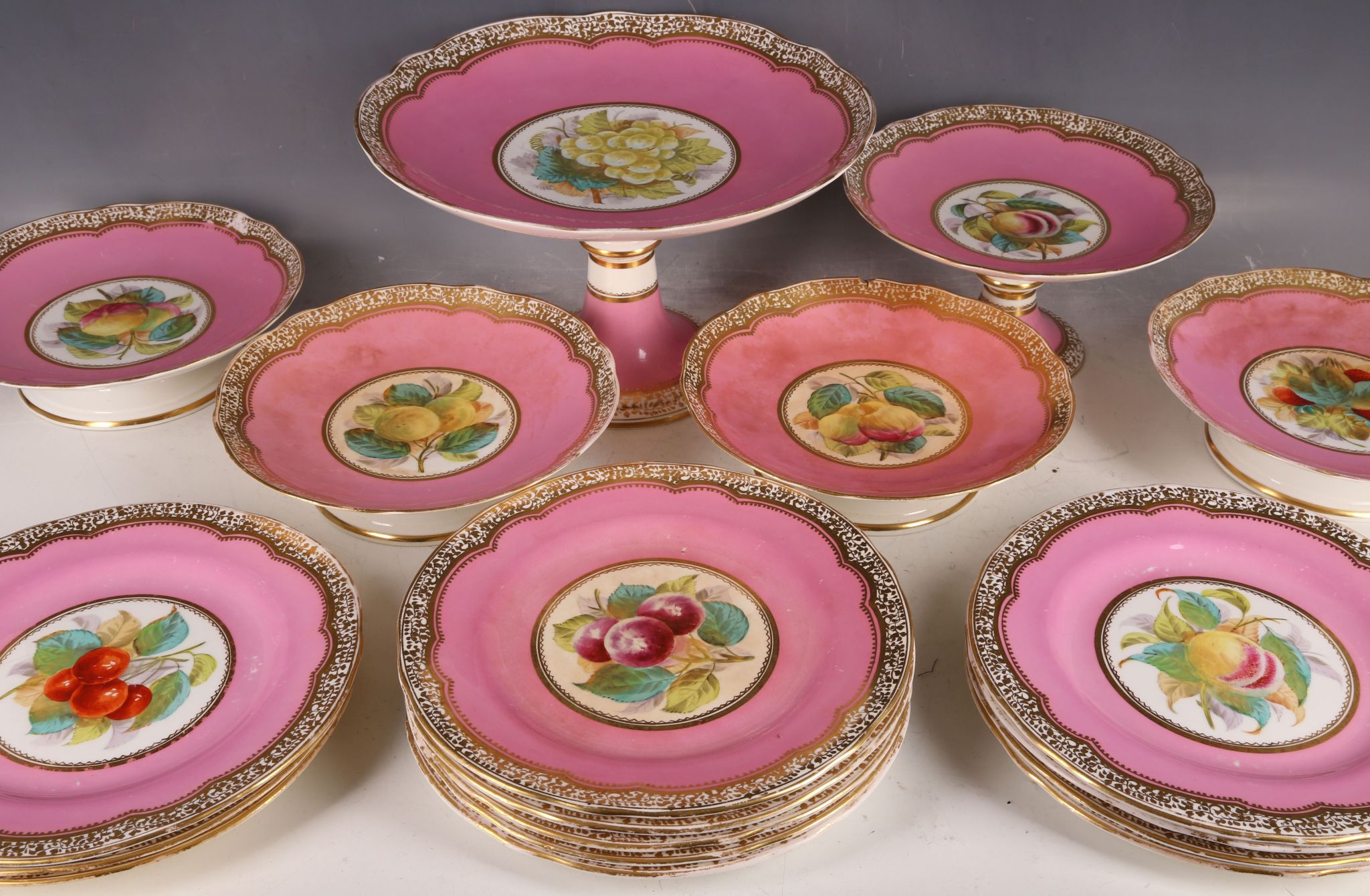 Twelve antique ceramic cake plates, decorated with fruits, pink and gilt frieze on white ground, and