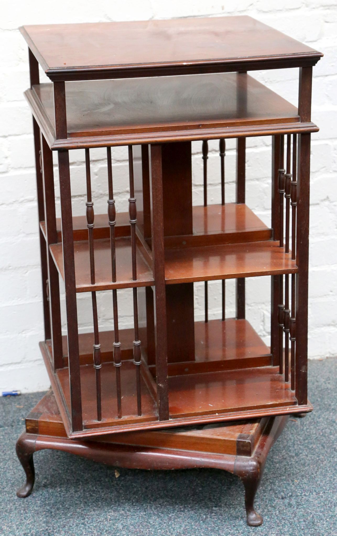 An antique mahogany revolving floor standing bookcase, with turned grill pillars and raised on squat