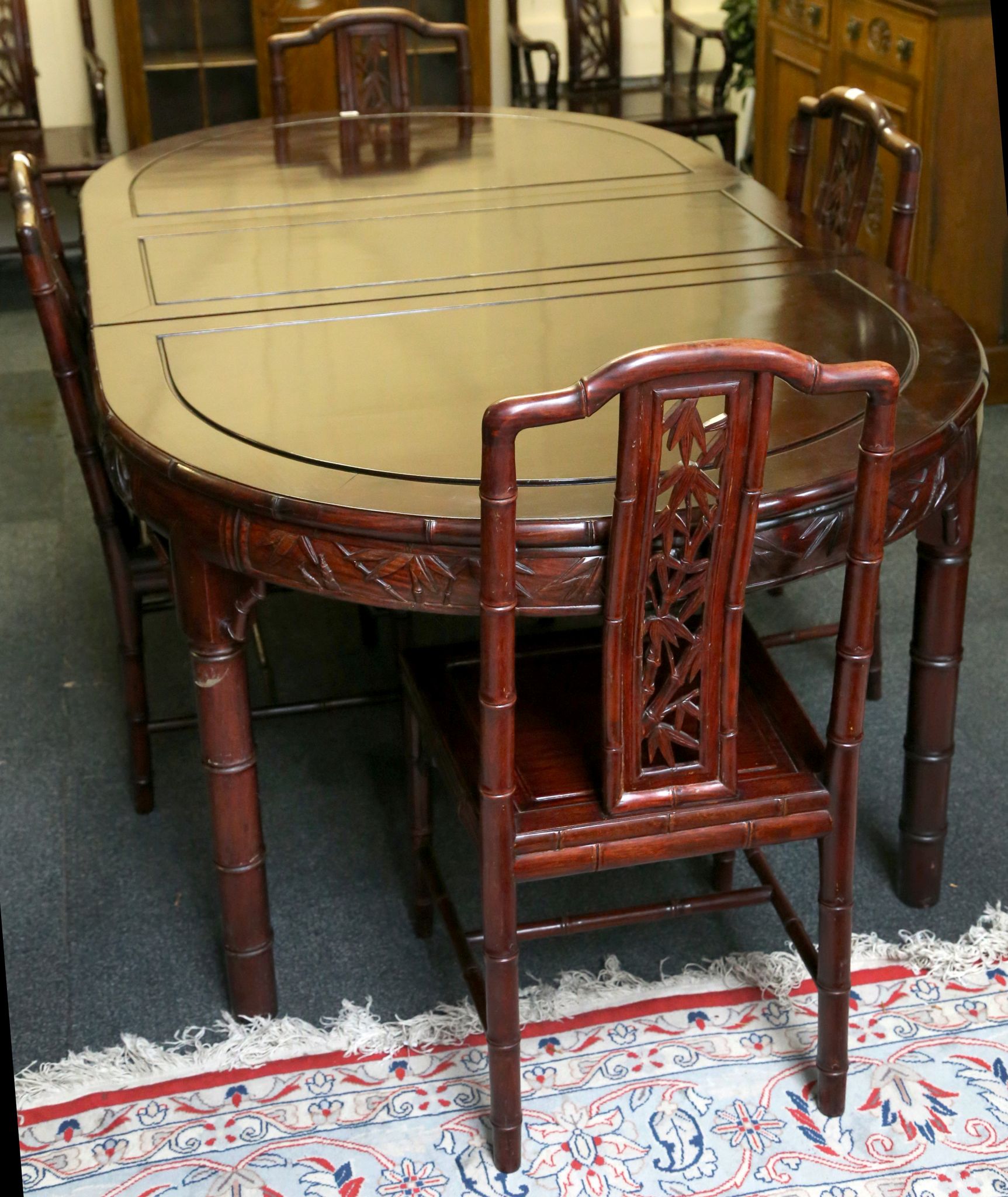 An Oriental hardwood oval dining table and six chairs, faux bamboo effect back and legs with