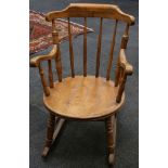 A stained beechwood rocking chair, with spindle back over a solid seat flanked by open arm rests,