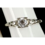 An 18ct white gold and diamond solitaire ring, the claw set central stone flanked by diamond