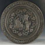 A Persian silvered roundel, modelled in bas relief and répoussage with a scene of a scholar and a